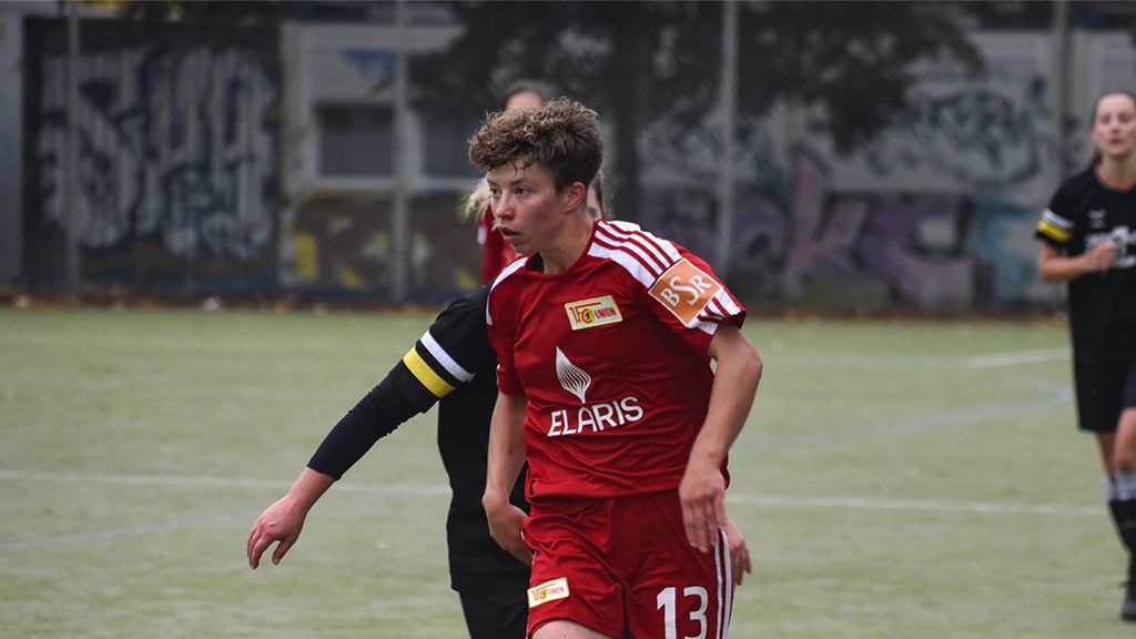 Ein Fußballspieler in einem roten Trikot mit der Nummer 13, auf einem Spielfeld im Freien, während eines Spiels.