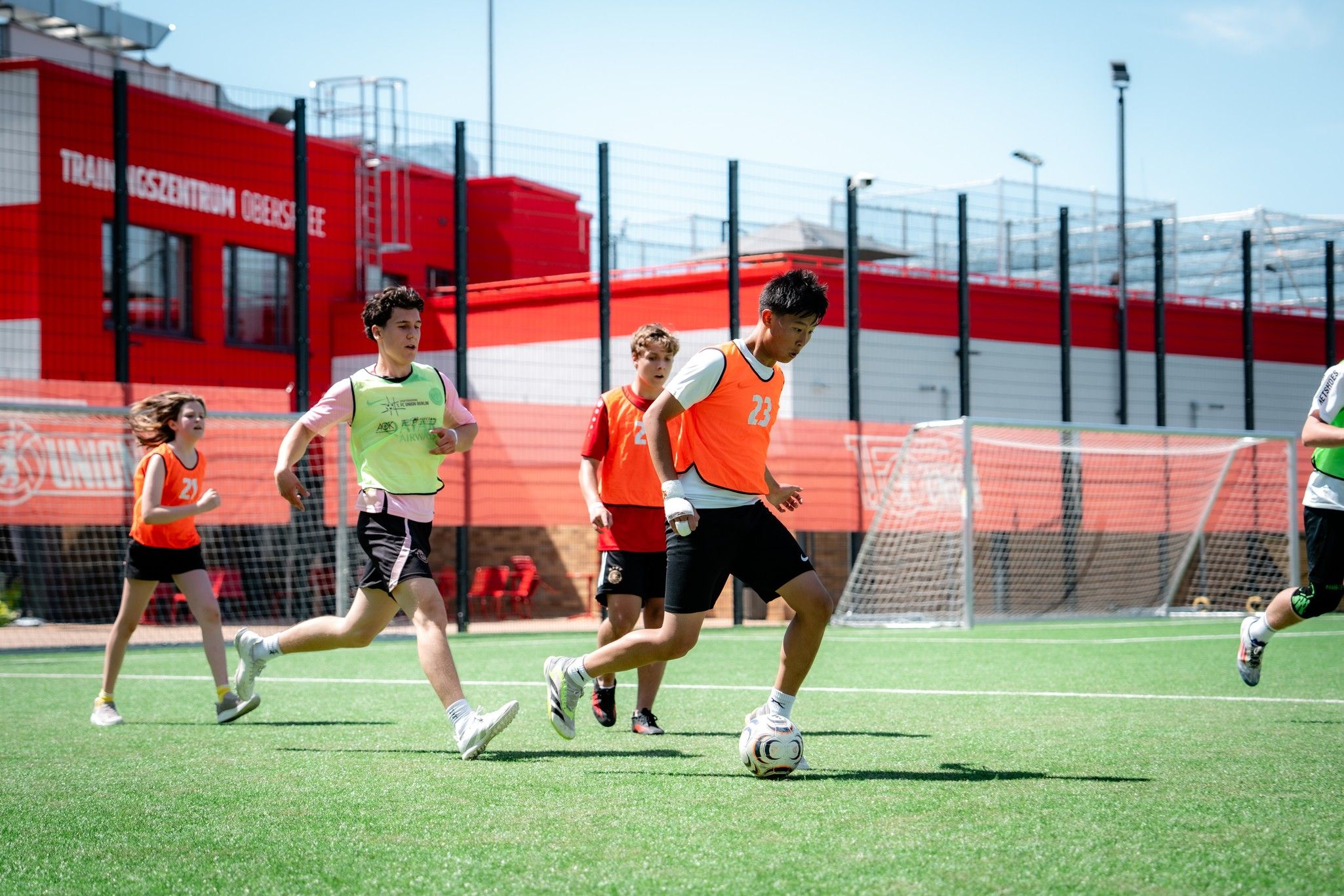 Spielende Jugendliche in Sportkleidung beim Fußballtraining auf einem Kunstrasenplatz.