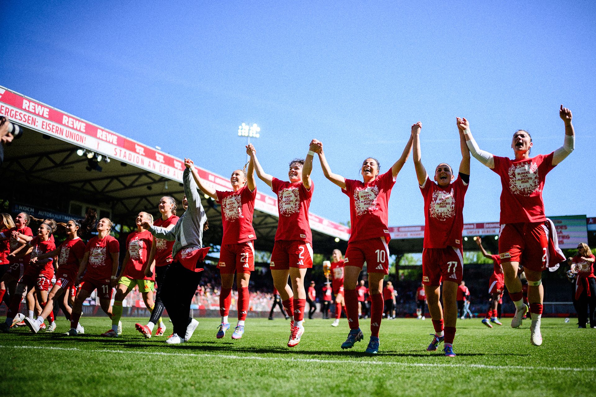 Feiernde Fußballspielerinnen in roten Trikots halten sich an den Händen, während sie den Sieg im Stadion feiern.