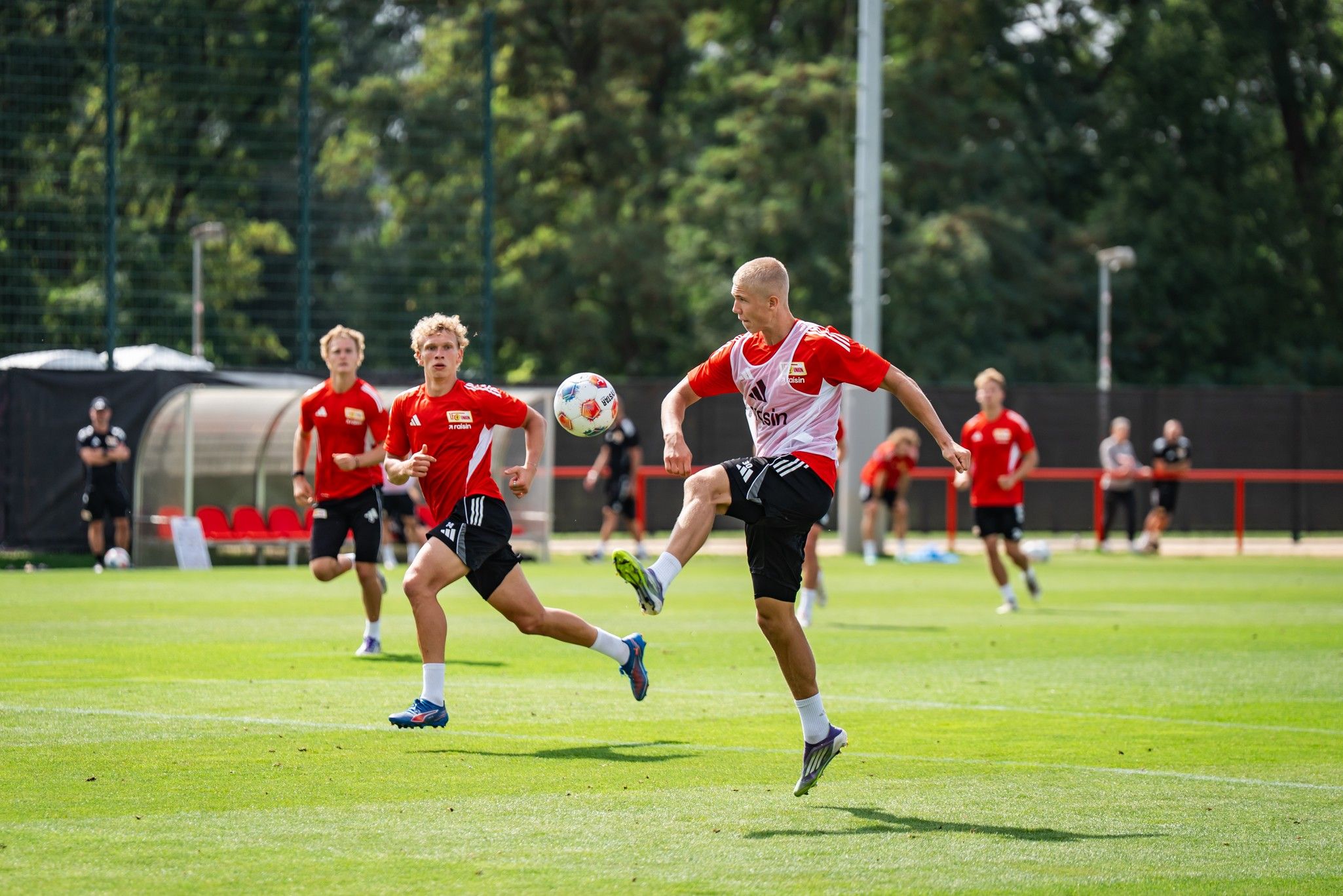 Fußballspieler trainieren auf einem Rasenplatz, ein Spieler führt einen Schuss aus, während andere zuschauen.