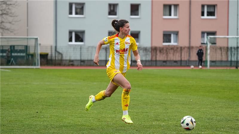 A female soccer player in a yellow uniform sprints across the field while chasing the ball.