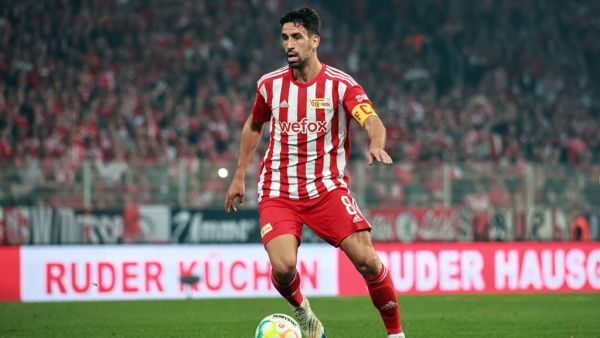 A football player in a red and white uniform with the number 8 and captain's armband, playing on a field.