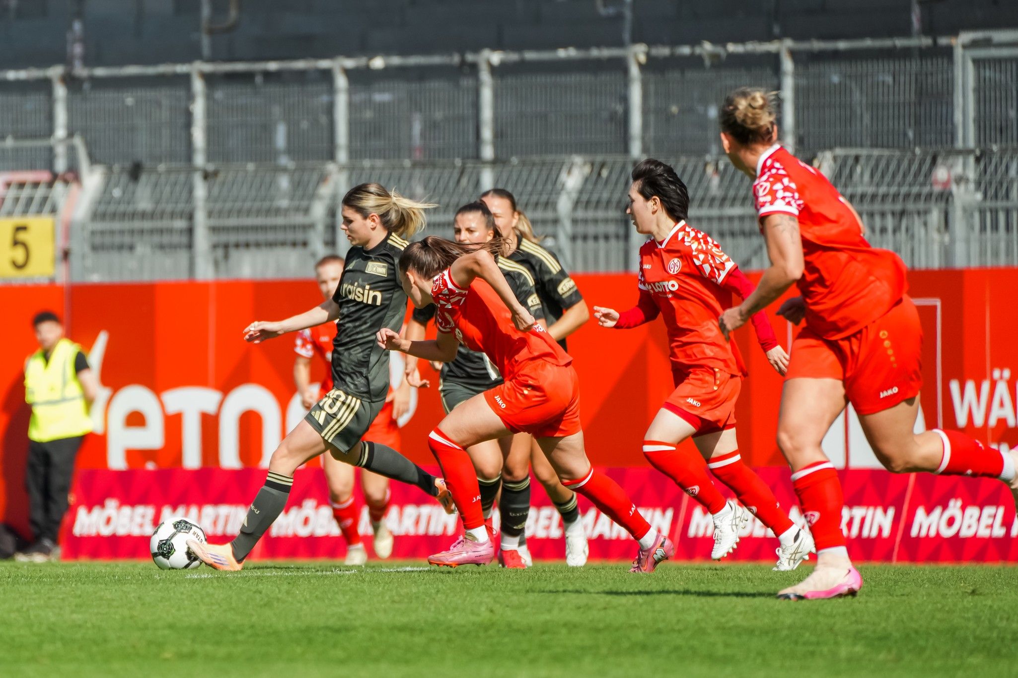 Spielszene eines Frauenfußballspiels mit Spielerinnen in schwarzen und roten Trikots, die um den Ball kämpfen.