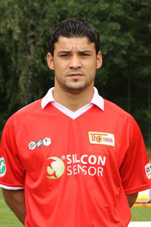 Ein Spieler in einem roten Fußballtrikot mit Logos steht vor einem unscharfen Hintergrund.