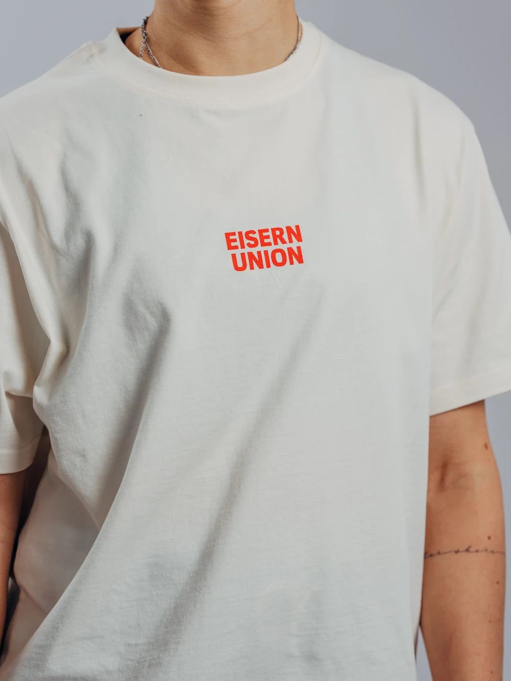 Weißes T-Shirt mit rotem Aufdruck "EISERN UNION" auf der Brust, getragen von einer Person im oberen Bildbereich.