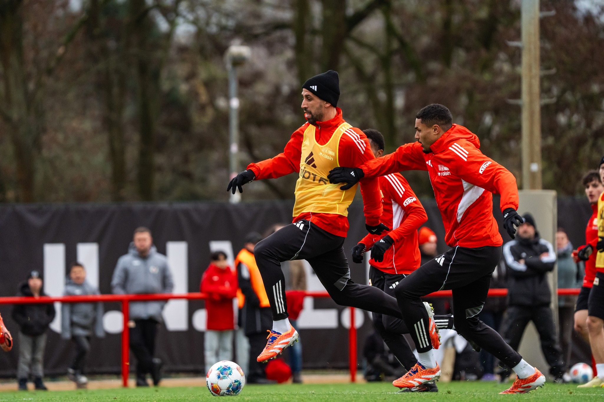 Spieler in Trainingskleidung üben im Freien, dabei ist einer in einem gelben Übungsleibchen und mehrere andere in roten Trikots.