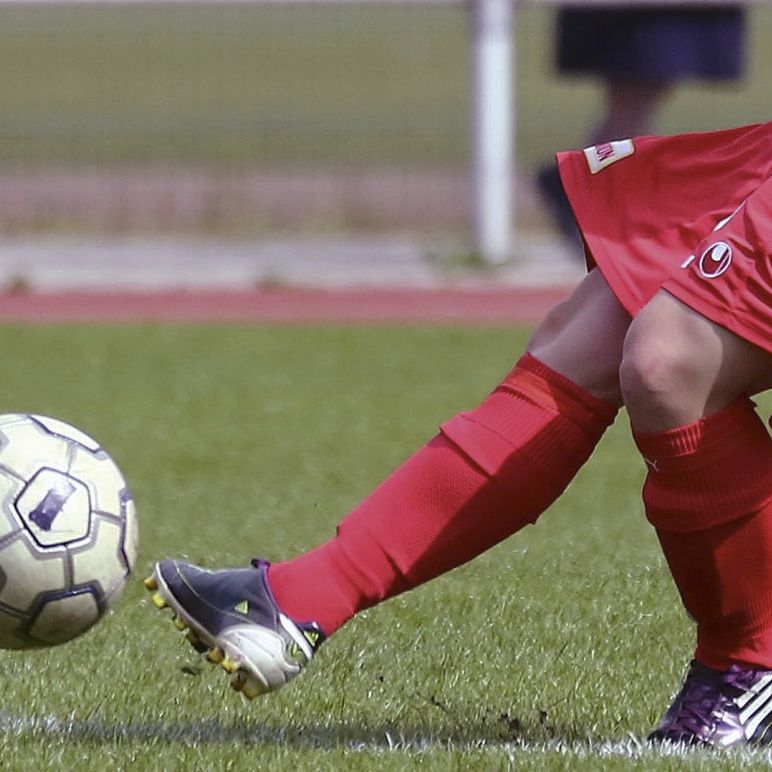 Ein Fußballspieler in roter Kleidung tritt einen Fußball auf einem grünen Rasenfeld.