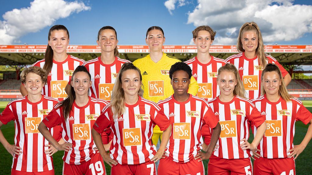 Eine Gruppe von zehn Fußballspielerinnen in rot-weiß gestreiften Trikots, posierend in einem Stadion mit blauem Himmel.