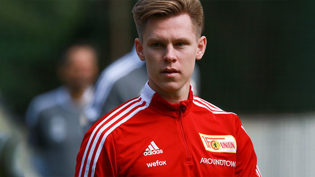 Ein junger Fußballspieler in einem roten Trainingsanzug mit dem Logo von Union Berlin, schaut konzentriert in die Kamera.
