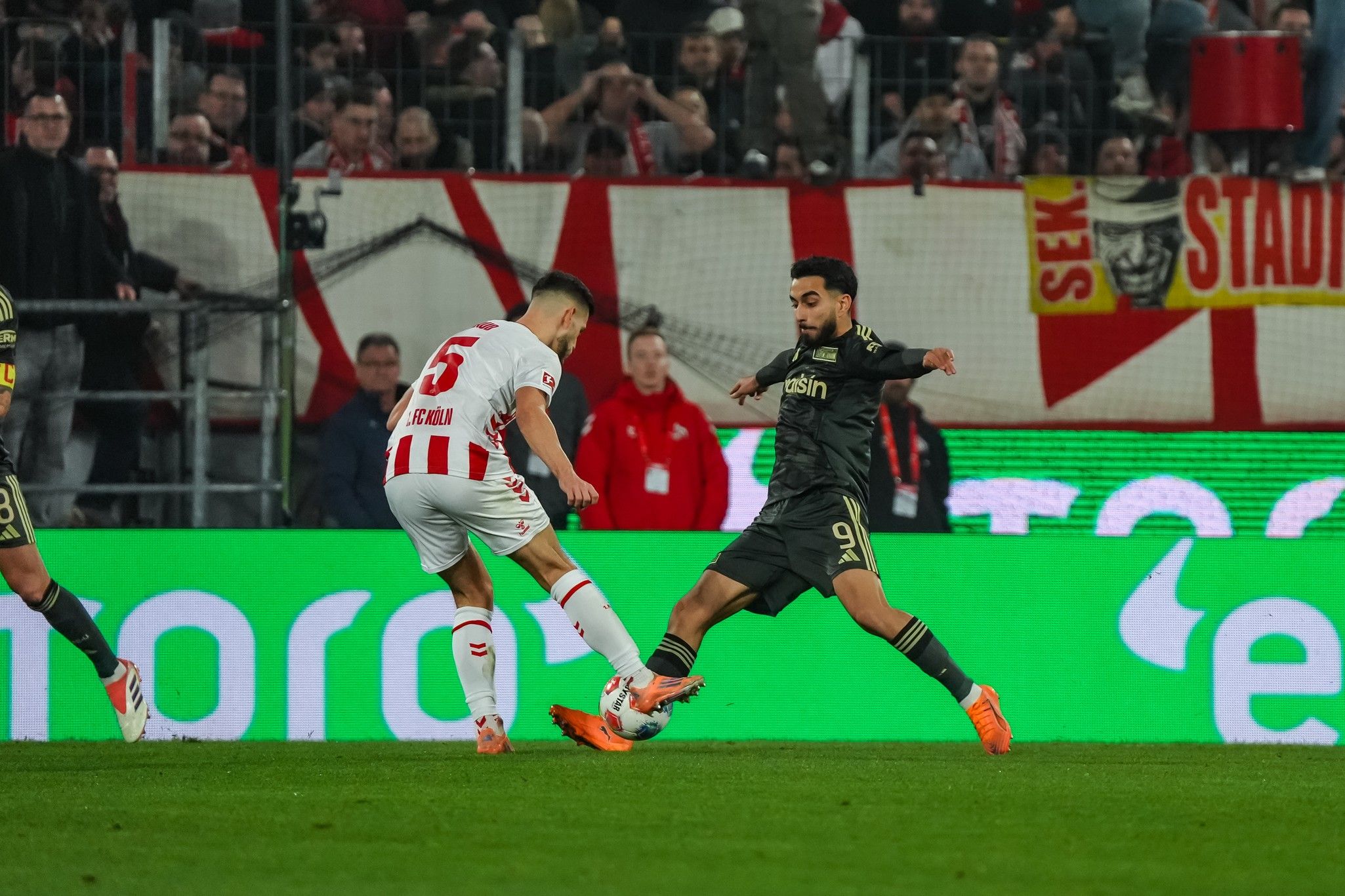 Zwei Fußballspieler in Aktion während eines Spiels, einer versucht den Ball zu stoppen, der andere ist im Dribbling.
