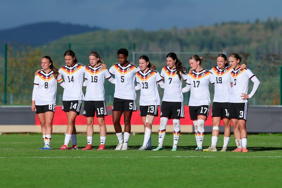 Eine Gruppe von weiblichen Fußballspielerinnen in Trikots mit deutschem Nationalflaggen-Motiv steht auf einem Fußballplatz.
