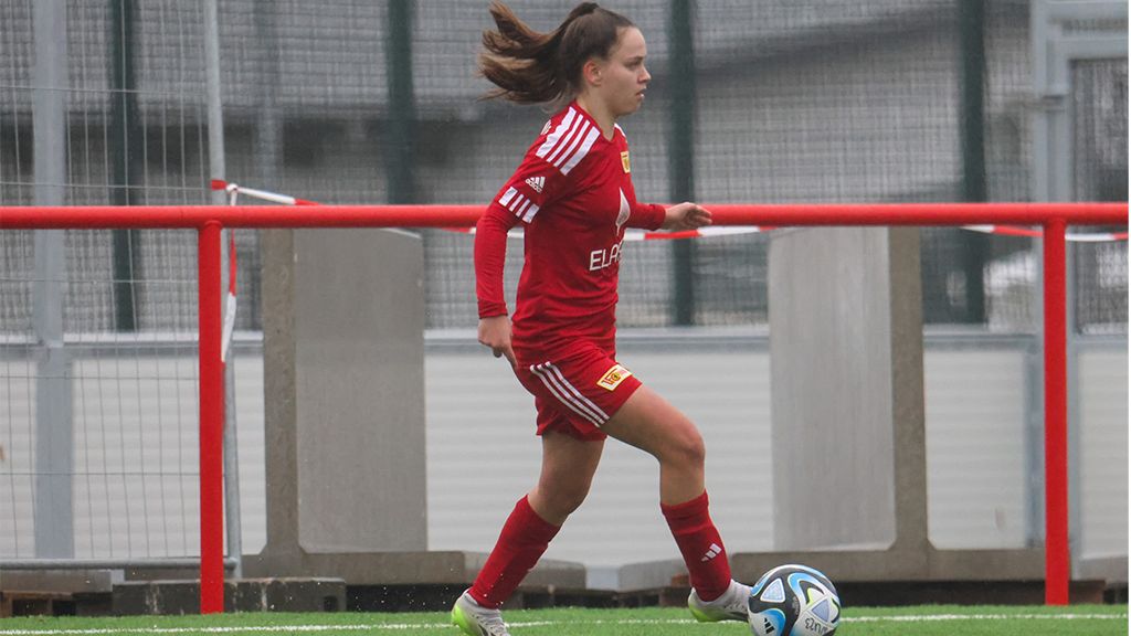 Eine Fußballspielerin in rotem Trikot läuft mit einem Ball auf dem Spielfeld.
