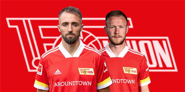 Zwei Fußballspieler in rot-weißen Trikots des 1. FC Union Berlin vor einem roten Hintergrund mit Vereinslogo.