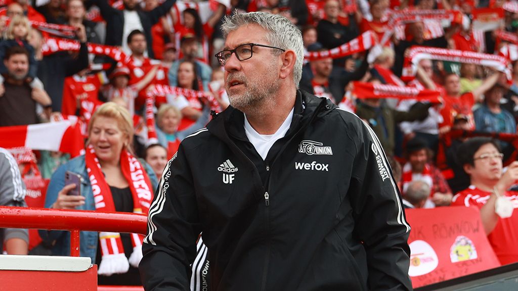 A coach stands on the bench, surrounded by fans supporting their team with scarves.