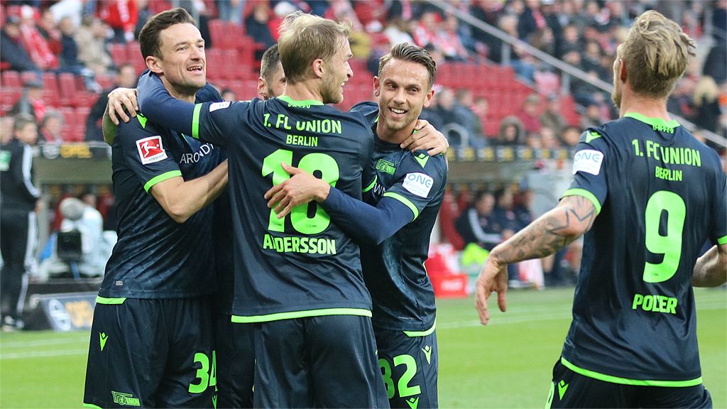 Spieler von Union Berlin feiern einen Torerfolg auf dem Spielfeld, umgeben von jubelnden Fans.