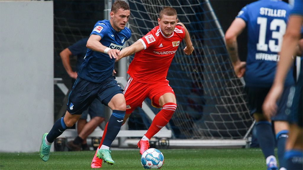 A soccer match with two players in action: one in blue and one in red gear, both with the ball.