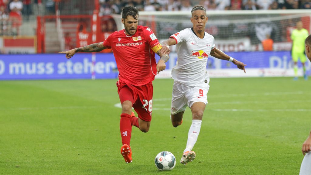 Zwei Fußballspieler in roten und weißen Trikots kämpfen um den Ball auf einem Spielfeld in einem Stadion.