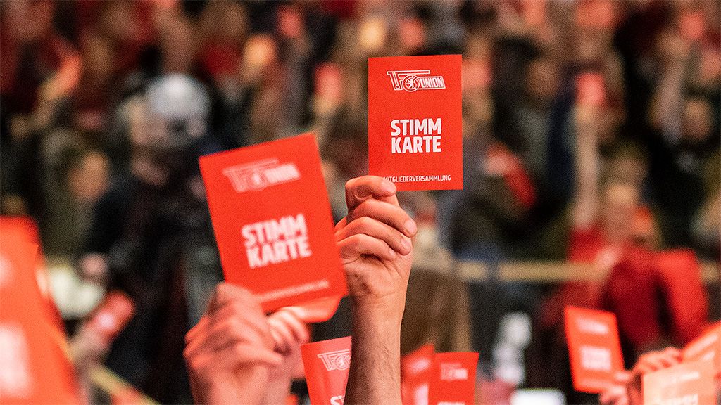 Hände halten rote Stimmkarten mit der Aufschrift "STIMM KARTE" während einer Veranstaltung.