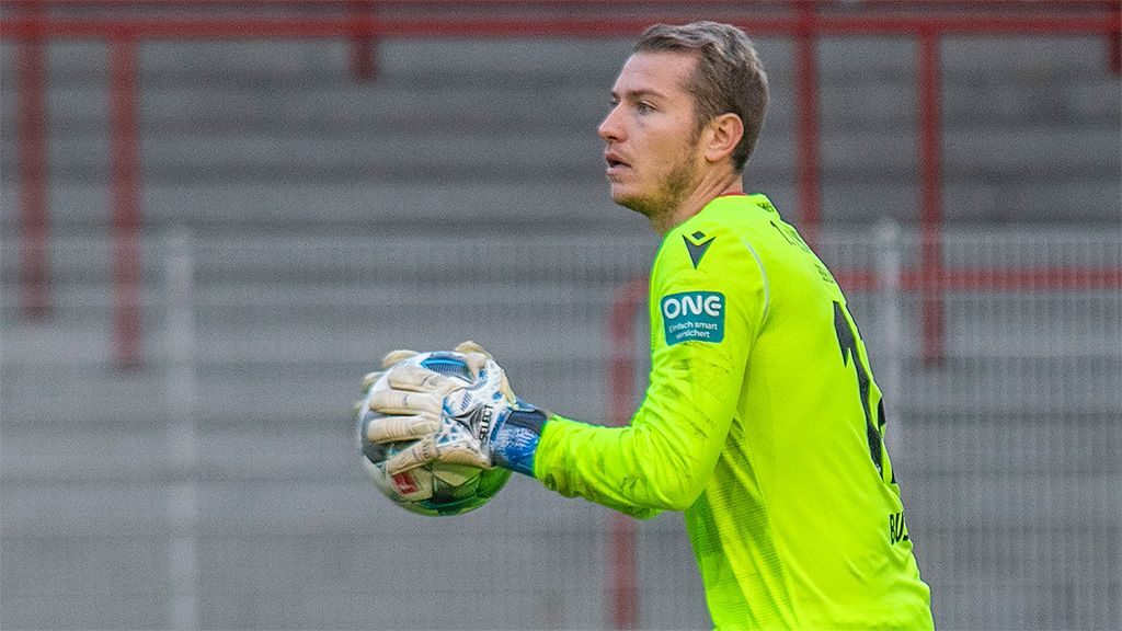 The goalkeeper in a bright green jersey catches the ball and looks attentively towards the field.