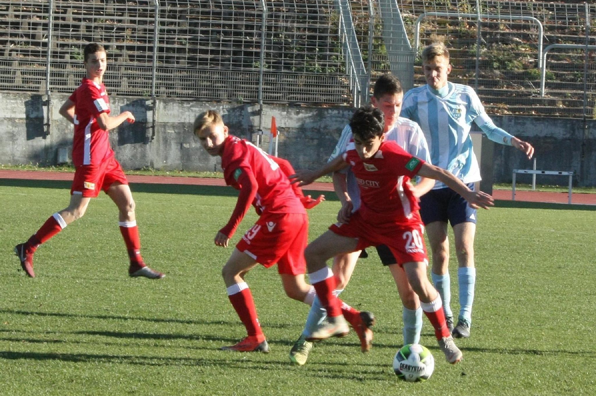Jugendfußballspiel mit Spielern in roten und blauen Trikots, die um den Ball kämpfen auf einem grünen Rasenplatz.