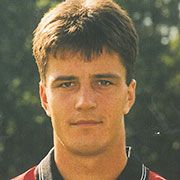 Junger Mann mit kurzen, dunklen Haaren und neutralem Gesichtsausdruck, aufgenommen im Freien.