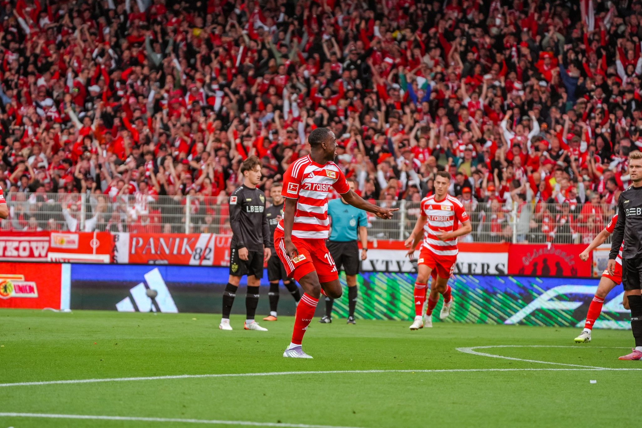 Ein Fußballspieler in rot-weißer Uniform jubelt vor einer jubelnden Menge im Stadion.