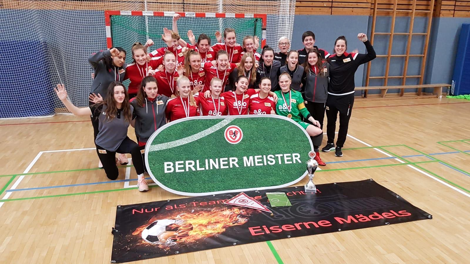 Gruppe von Frauen in Sportkleidung, die nach einem Sieg feiern, stehen vor einem Banner mit der Aufschrift "Berliner Meister".