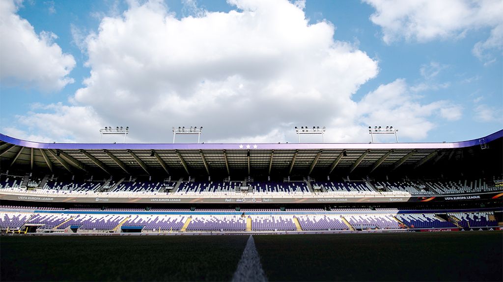 Empty stadium view with seats and blue sky, clouds over the field and floodlights in the background.