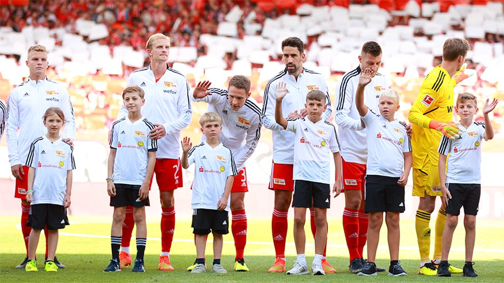 Fußballmannschaft von Union Berlin steht mit Kindern auf dem Platz, bereit für ein Spiel.