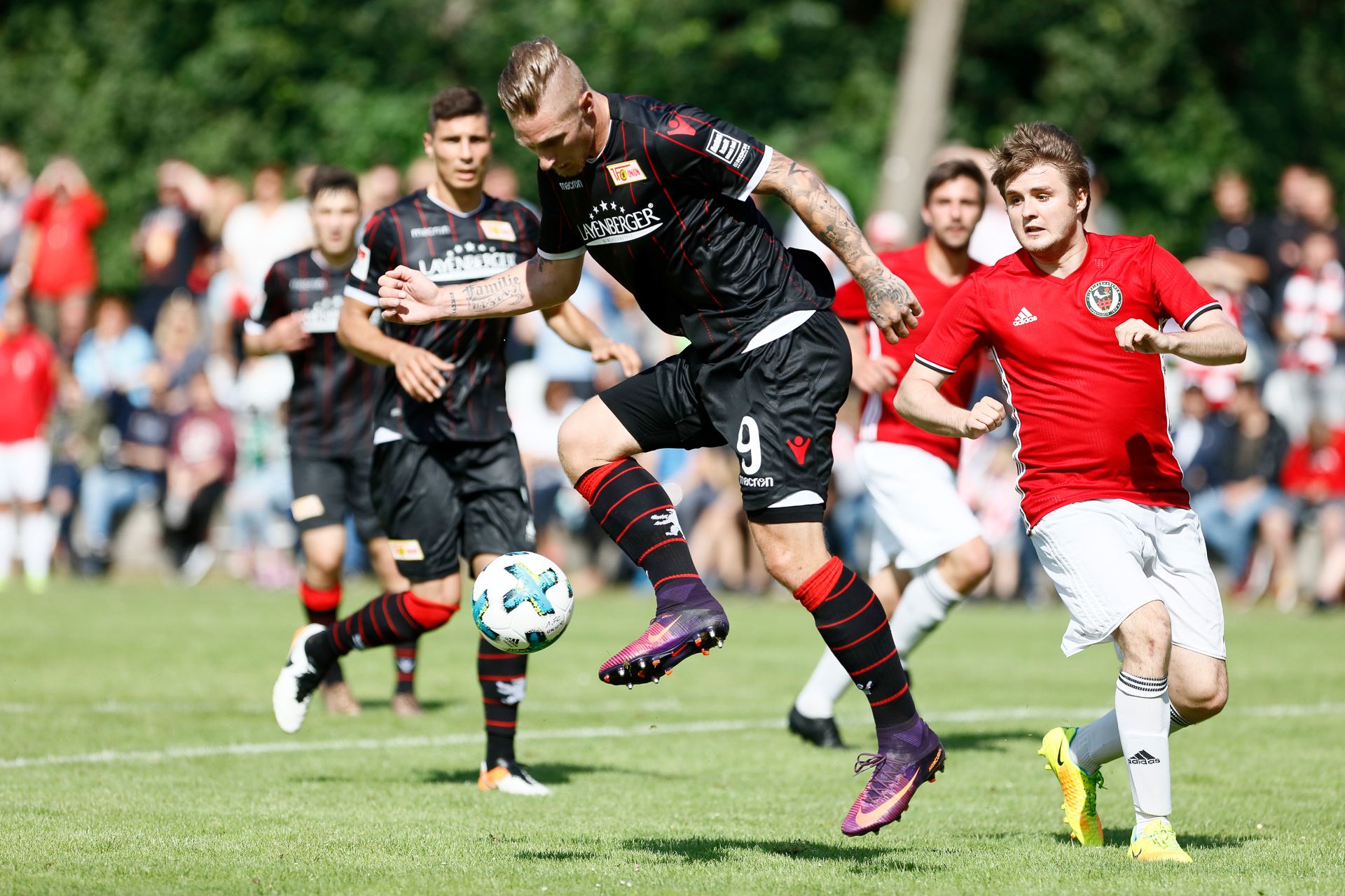 Spielszene eines Fußballspiels mit zwei Mannschaften. Ein Spieler springt, um den Ball zu erreichen, während ein Gegner ihn verfolgt.