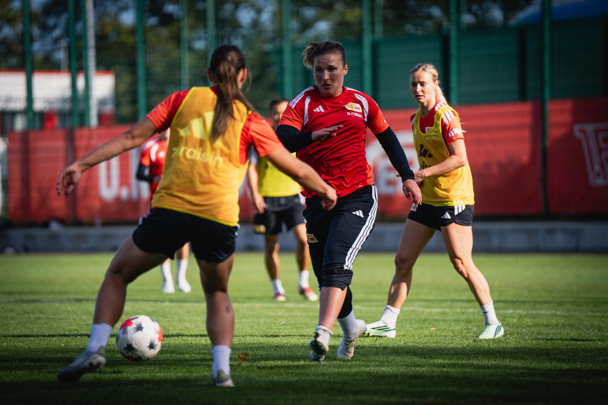 Frauenfußballmannschaft beim Training auf dem Rasen, Spielerinnen in roten und gelben Trikots.