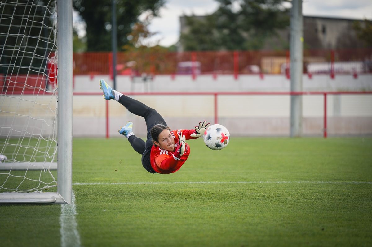 Eine Torhüterin springt im Fußball, um den Ball zu halten, während sie mit beiden Händen danach greift.