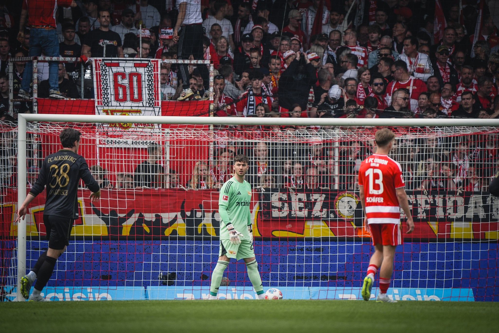 Fußballspiel mit Torhüter in Aktion, Fans im Hintergrund, die ein Stadionbanner halten.