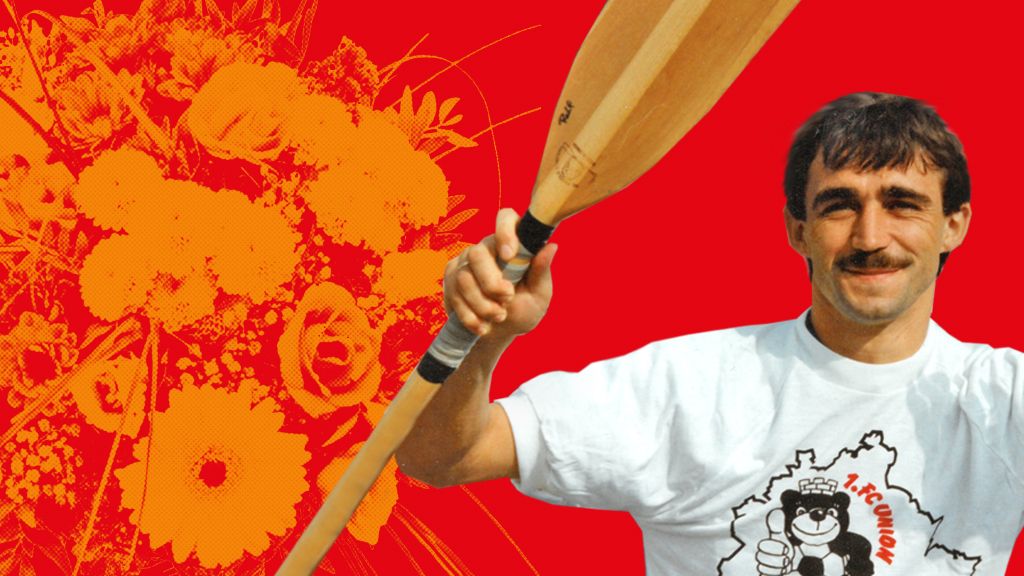 Ein Mann mit Schnurrbart und Paddel in der Hand trägt ein T-Shirt mit einem Bären-Logo, vor einem roten Hintergrund mit Blumenmotiven.