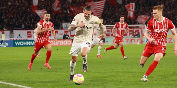 Fußballspiel. Spieler in roten und weißen Trikots. Sie laufen zum Ball. Zuschauer freuen sich und jubeln.