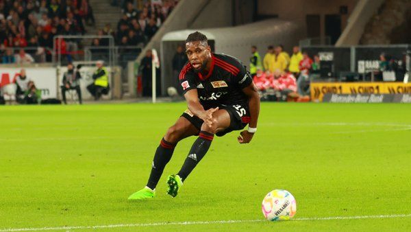 A soccer player in a black jersey sprints across the field while controlling the ball.