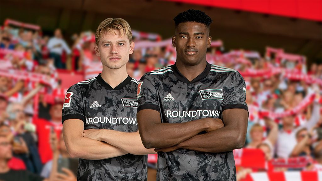 Two football players in black-gray jerseys stand with crossed arms in front of a cheering crowd in the background.