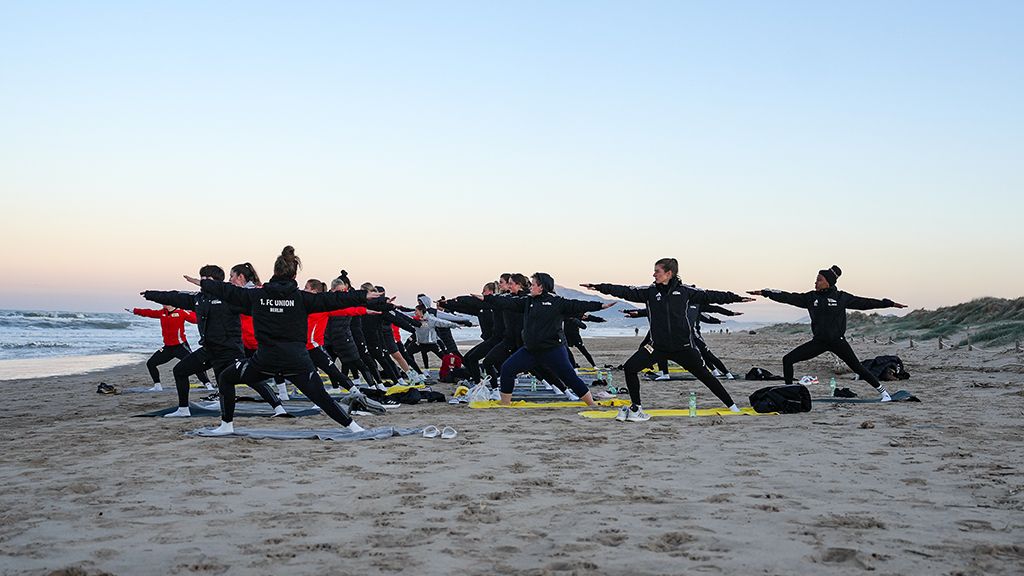 Eine Gruppe von Menschen macht Yoga-Übungen am Strand bei Sonnenuntergang.