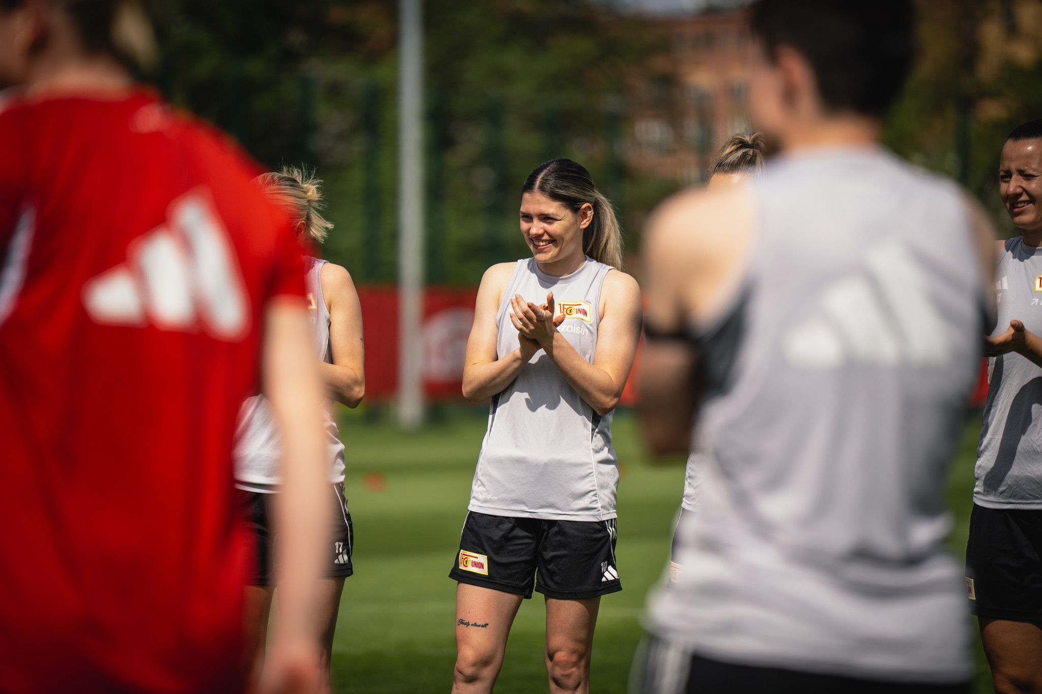 Eine Gruppe von Frauen in Sportbekleidung, die in einem Trainingsfeld stehen. Eine Spielerin klatscht lächelnd.