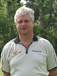 Eine Person mit grauen Haaren steht vor einem unscharfen grünen Hintergrund, trägt ein helles Polohemd und schaut direkt in die Kamera.