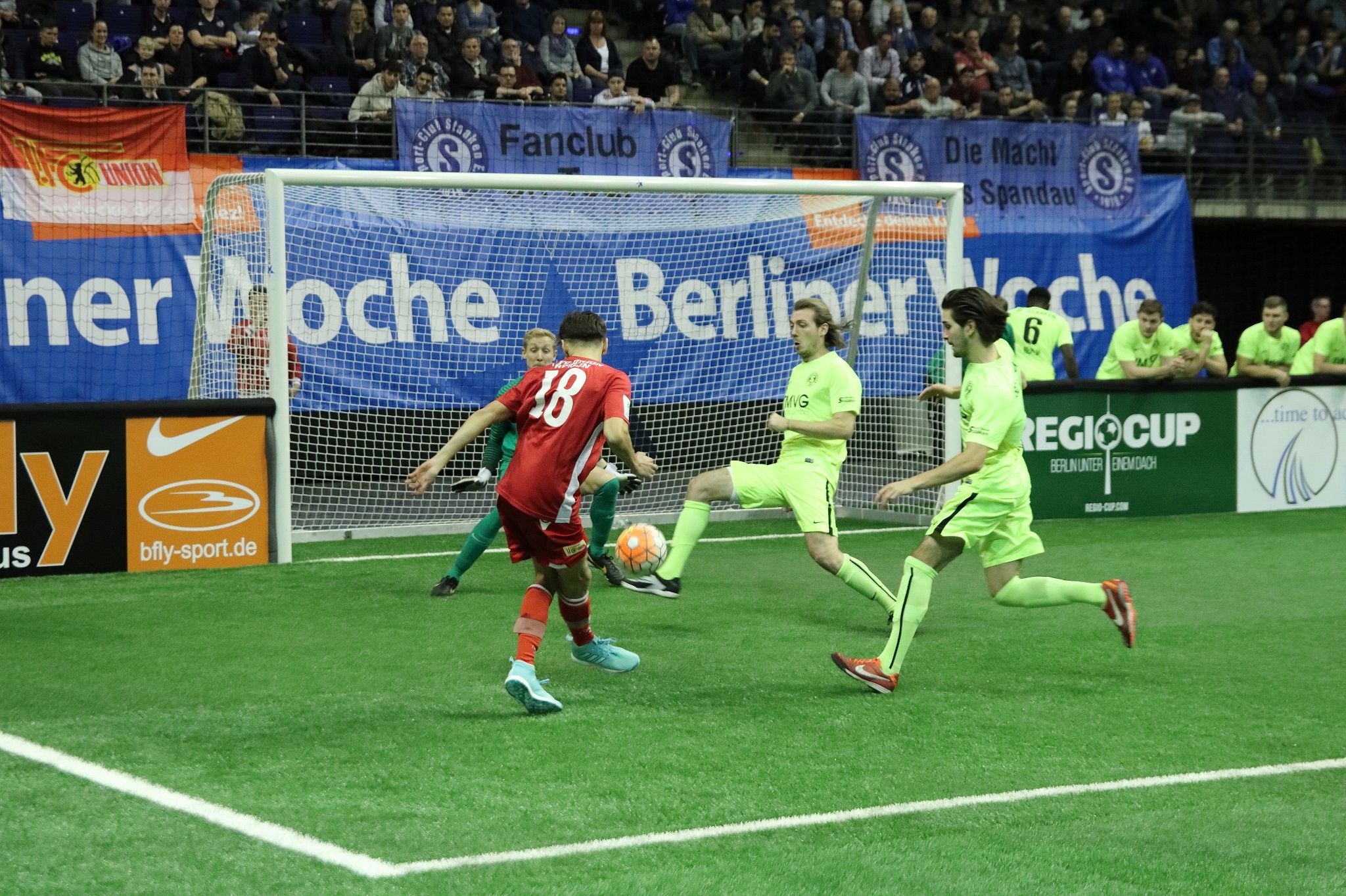 Ein Fußballspiel mit Spielern in roten und grünen Trikots, die sich um den Ball im Torbereich drängen.