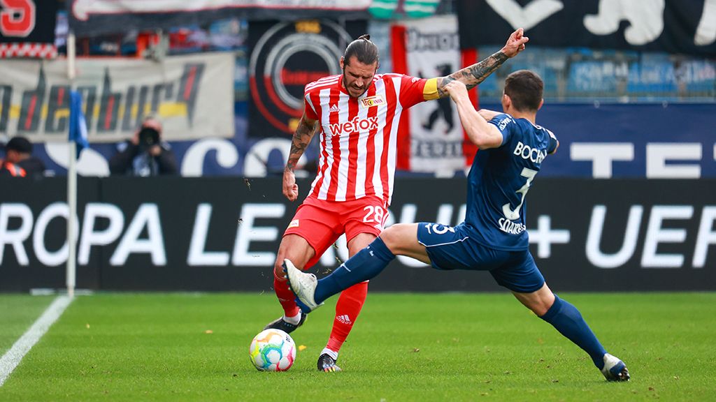 Game scene in football: A player in a red and white jersey is dribbling while an opponent tries to stop him.