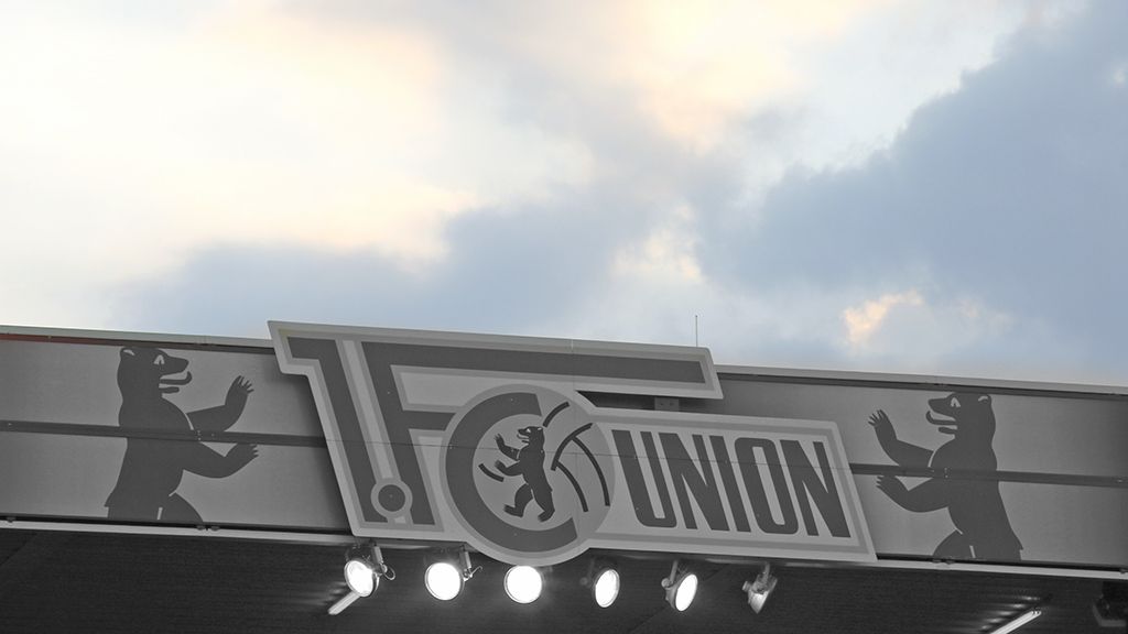 Logo von FC Union Berlin mit Bärenmotiven, umgeben von einer leicht bewölkten Himmelsszene.