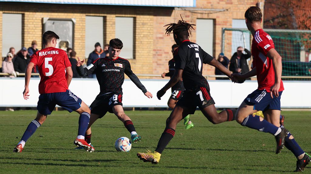 Ein Jugendfußballspiel, bei dem Spieler in roten und schwarzen Trikots um den Ball kämpfen.