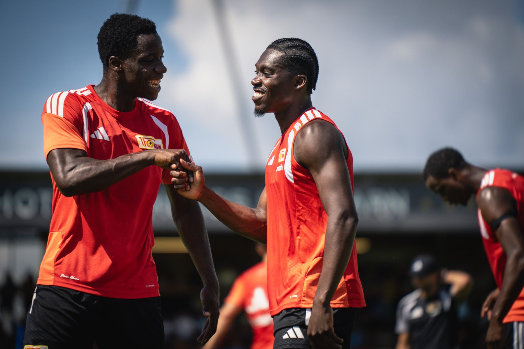 Zwei lächelnde Fußballspieler in roten Trikots stehen sich gegenüber und schütteln sich die Hände während des Trainings.