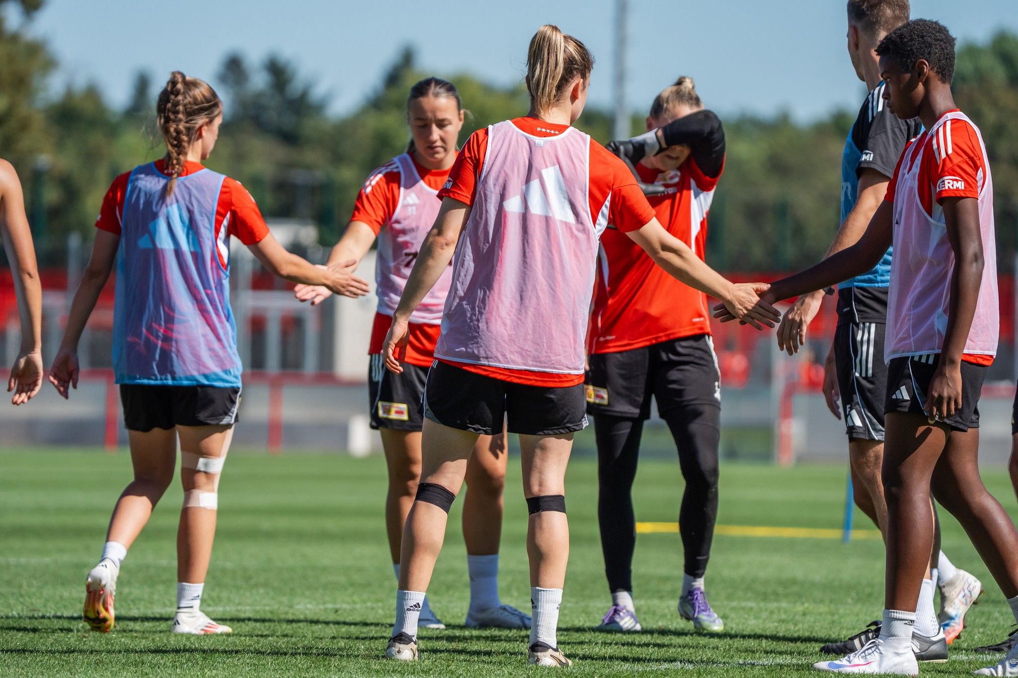 Gruppentraining von Fußballspielerinnen in roten Trikots, die sich auf dem Platz begrüßen.