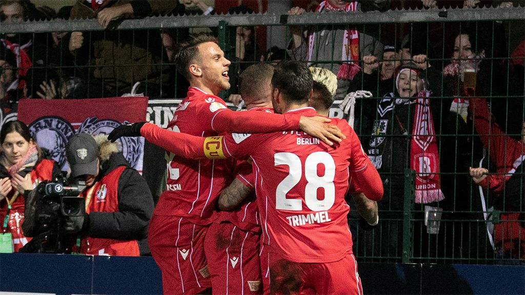 Union Berlin players celebrate a goal in front of cheering fans in the stadium.