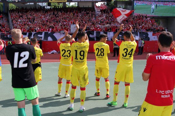 Spieler des 1. FC Union Berlin applaudieren den Fans in gelben Trikots, im Hintergrund jubelnde Zuschauer mit Fahnen.