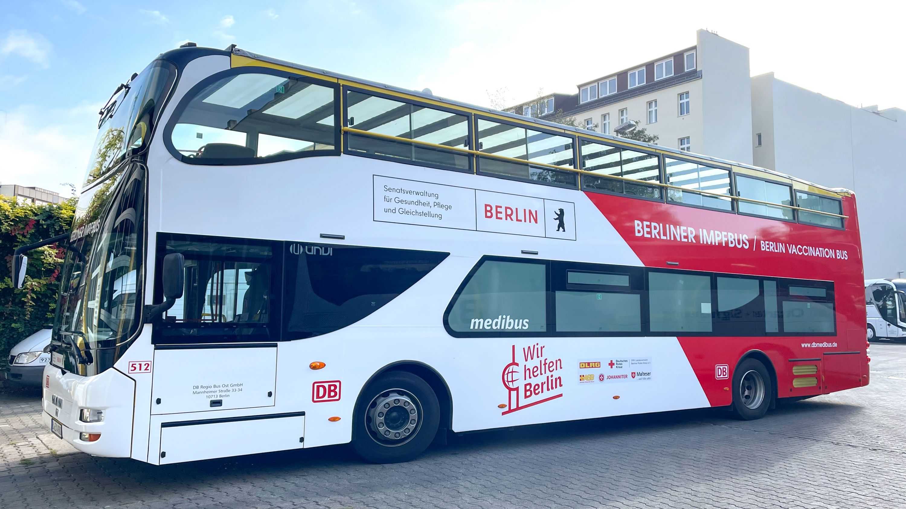Double-decker bus with advertising for Berlin and a social aid project, parked in a square.