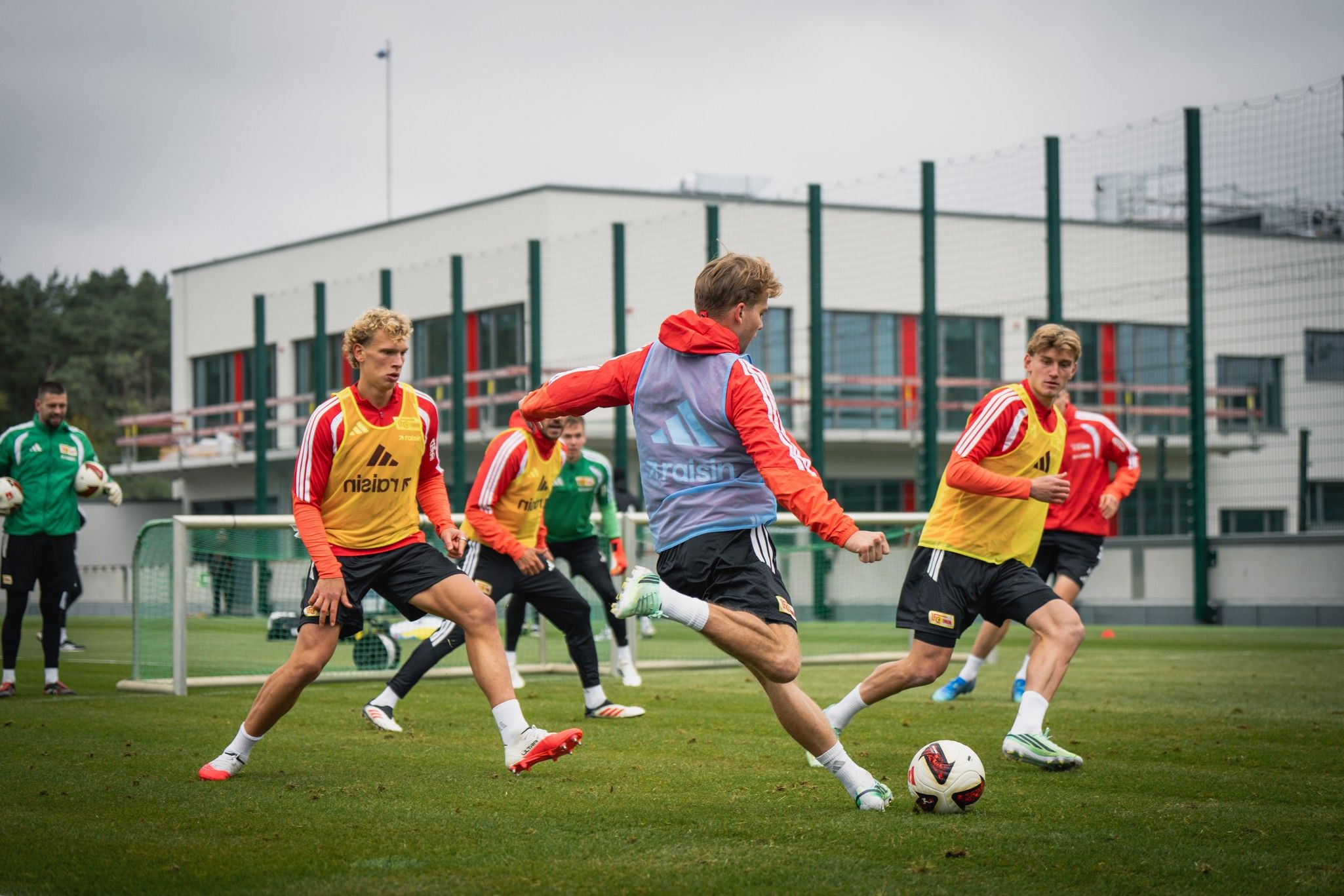 Fußballspieler trainieren auf einem Platz, während ein Spieler den Ball schießt und andere ihn umgeben.